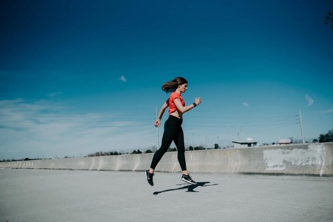 New Year's Resolution? You don't need one. This is an image of a woman in a red top and black pants (workout attire) running along pavement with a blue sky behind her.