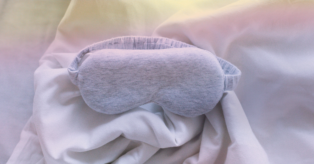 A grey sleeping masks rests on top of a bed top.